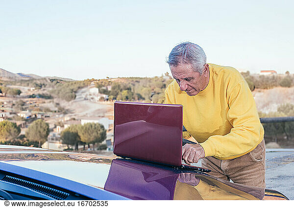 Ein älterer Mann benutzt einen Laptop auf der Motorhaube seines Autos