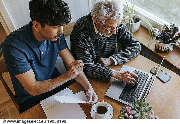 Ein älterer Mann benutzt einen Laptop  während er neben einem männlichen Betreuer sitzt  der medizinische Berichte zu Hause erklärt