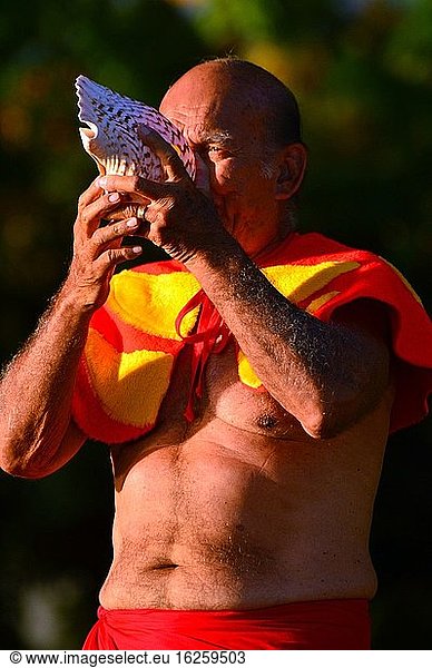 Ein älterer Mann bläst eine Muschel  um den Beginn eines traditionellen hawaiianischen Festes durch das Blasen einer Muschel zu signalisieren.
