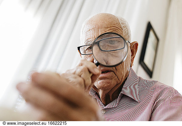 Ein älterer Mann im Ruhestand betrachtet ein Fossil durch ein Vergrößerungsglas