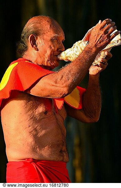 Ein Ältester signalisiert den Beginn der Feierlichkeiten auf Hawaii  indem er in eine Muschelschale bläst.