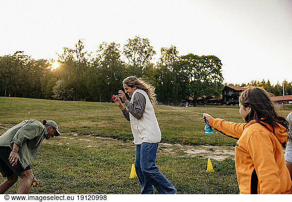 Ein Mädchen bespritzt eine Betreuerin mit Wasser  während sie auf dem Spielplatz eines Ferienlagers Spaß hat