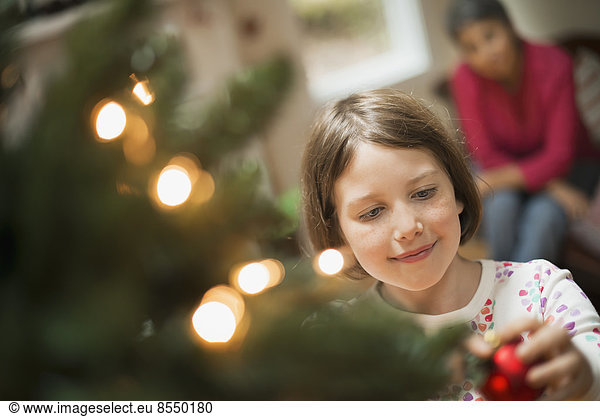 Ein Mädchen  das einen handgemachten Schmuck an einem Weihnachtsbaum platziert.