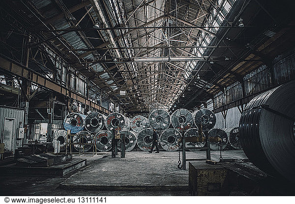 Ein männlicher Arbeiter geht in voller Länge an Stahlblechen in der Fabrik vorbei