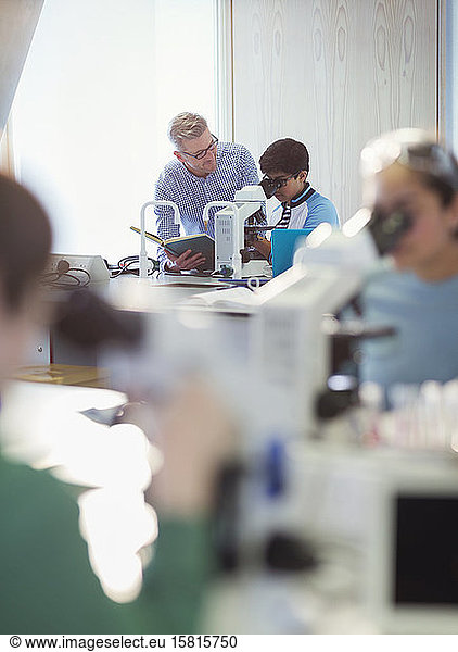 Ein männlicher Lehrer und ein Schüler benutzen ein Mikroskop und führen ein wissenschaftliches Experiment in einem Klassenzimmer durch
