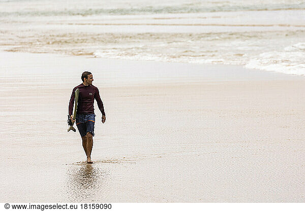Ein männlicher Surfer geht mit Surfbrett am Strand spazieren