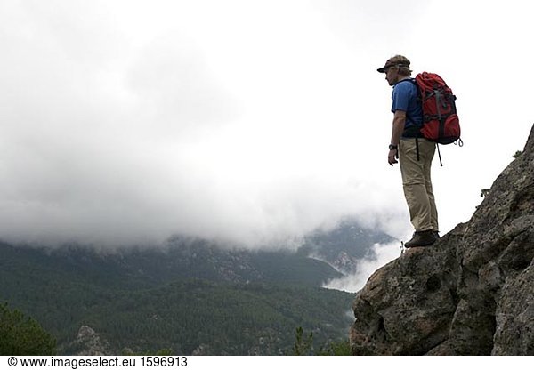 Ein Mann auf einem Felsvorsprung in einer Felswand in Wolken stehend.