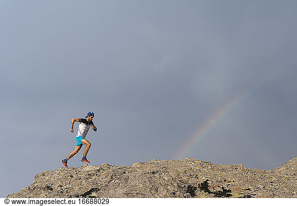 Ein Mann beim Trailrunning auf einem felsigen Gelände mit einem Regenbogen