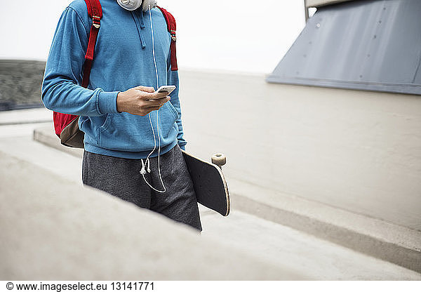 Ein Mann benutzt ein Mobiltelefon  während er auf einem Parkplatz ein Skateboard trägt