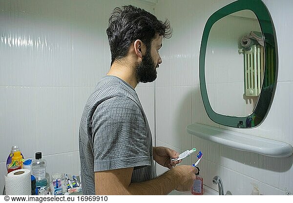 Ein Mann bereitet sich vor einem Spiegel auf das Zähneputzen vor  und sein Spiegelbild erscheint darauf.