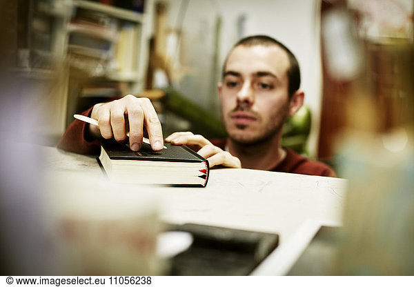 Ein Mann  der ein Handwerkzeug auf dem Einband eines Buches benutzt.