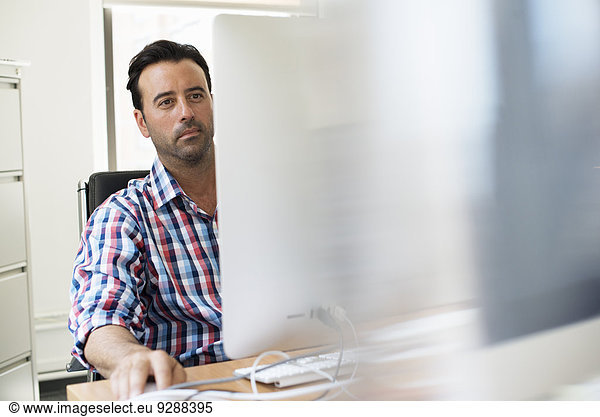 Ein Mann  der in einem Büro an einem Schreibtisch mit einem Computer arbeitet.
