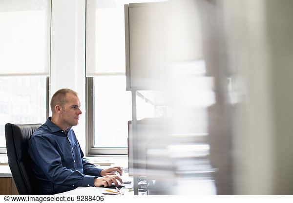 Ein Mann  der in einem Büro an einem Schreibtisch mit einer Computermaus arbeitet. Er konzentriert sich auf eine Aufgabe.