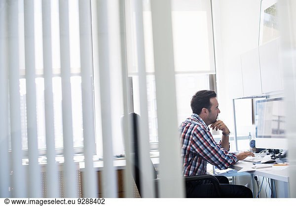 Ein Mann  der in einem Büro arbeitet und sich auf eine Aufgabe konzentriert. Er benutzt eine Computertastatur und einen Bildschirm.
