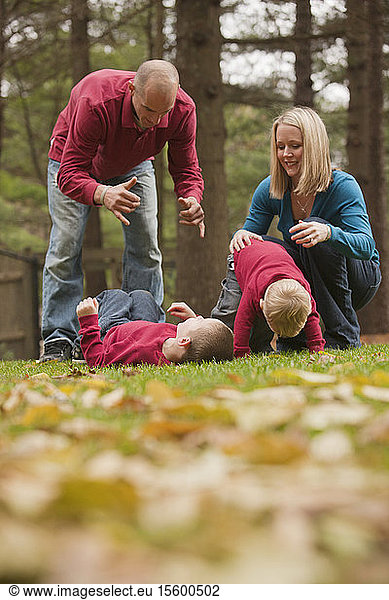 Ein Mann gebärdet das Wort Play in amerikanischer Gebärdensprache  während er mit seinem Sohn in einem Park spielt