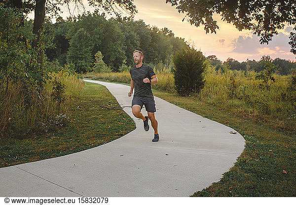 Ein Mann joggt bei Sonnenuntergang in der Natur allein auf einem baumgesäumten Pfad