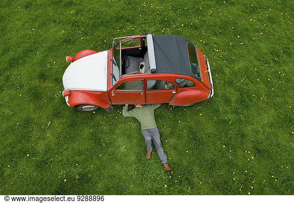 Ein Mann liegt auf dem Rücken unter einem roten Auto und inspiziert die Unterseite des Wagens.