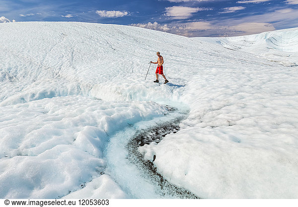 Ein Mann ohne Hemd im Badeanzug läuft mit Trekkingstöcken über die Oberfläche des Root Glacier im Wrangell-St. Elias National Park; Alaska  Vereinigte Staaten von Amerika
