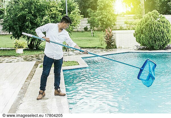 Ein Mann reinigt Pool mit Laubsauger. Mann reinigt den Pool mit dem Skimmer  Person mit Skimmer Reinigung Pool  Hände halten einen Skimmer mit blauen Pool im Hintergrund