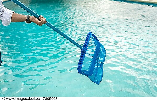 Ein Mann reinigt Pool mit Laubsauger. Mann reinigt den Pool mit dem Skimmer  Person mit Skimmer Reinigung Pool  Hände halten einen Skimmer mit blauen Pool im Hintergrund