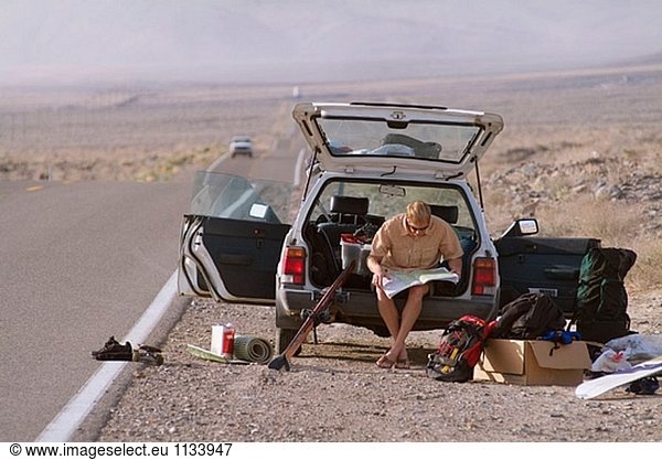 Ein Mann sitzt auf Heckklappe Autos in der Wüste