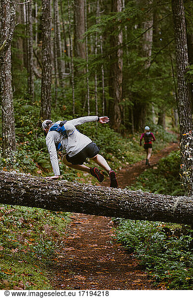 Ein Mann springt beim Trailrunning mit einem Freund über einen umgestürzten Baum