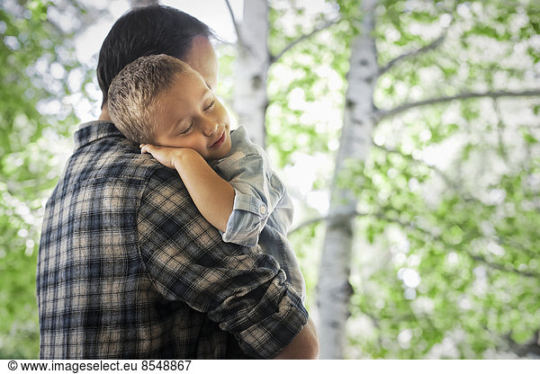 Ein Mann wiegt ein schlafendes Kind und ruht auf seiner Schulter.
