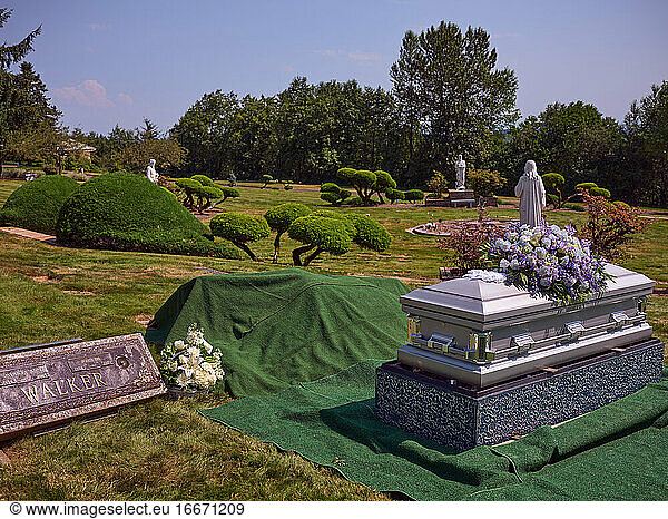 Ein mit Blumen geschmückter Sarg steht neben einer Grabstätte bereit für die Beisetzung.