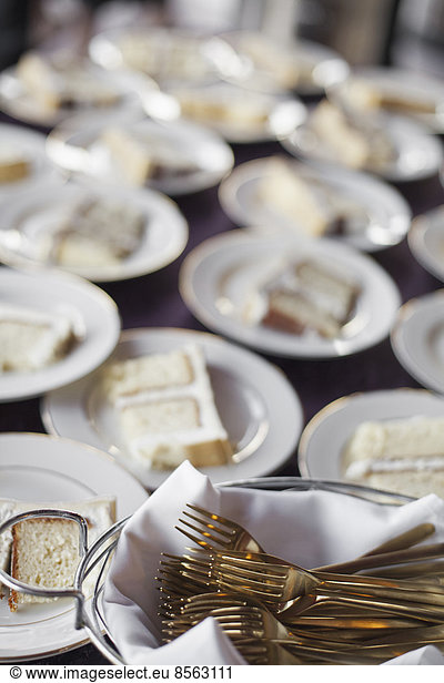 Ein mit Tellern beladener Tisch. Weißes Porzellan und ein Korb voller Dessertgabeln. Ein Stück Hochzeitstorte.