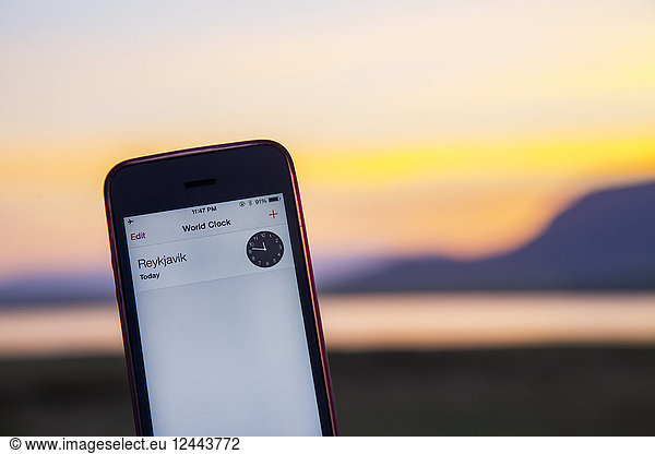 Ein Mobiltelefon zeigt die Ortszeit in Reykjavik kurz vor Mitternacht an  wobei das Tageslicht zur Sommersonnenwende noch sichtbar ist  wenn die Sonne in Island selbst um Mitternacht nicht vollständig untergeht  Reykjavik  Island