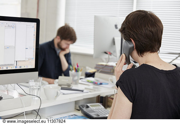 Ein moderner Büroarbeitsplatz. Eine Frau am Telefon und ein Mann  der sich auf eine Aufgabe konzentriert.
