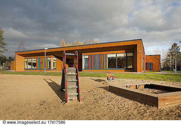 Ein modernes Gebäude  ein Kindergarten oder eine Vorschule  ein großer Sandspielplatz mit einer Rutsche.
