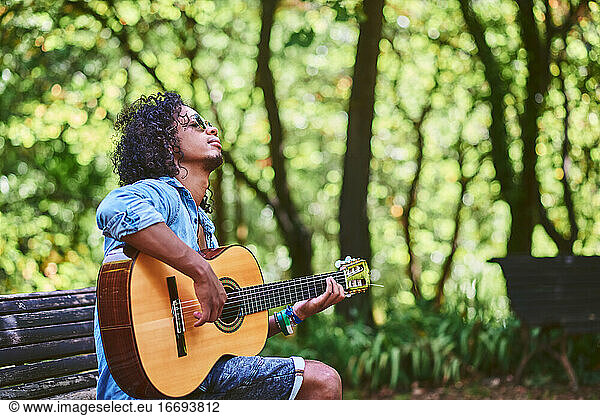 Ein Musiker spielt Gitarre in einem schönen Park. Er ist von Vegetation umgeben.