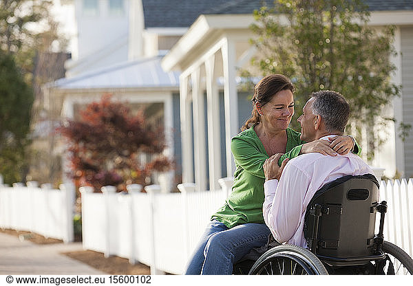 Ein Paar genießt die Gesellschaft des anderen vor seinem Haus  während er im Rollstuhl sitzt