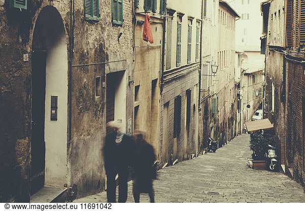 Ein Paar  Mann und Frau  die eine steile  gepflasterte Gasse in der Stadt Siena hinaufgehen.