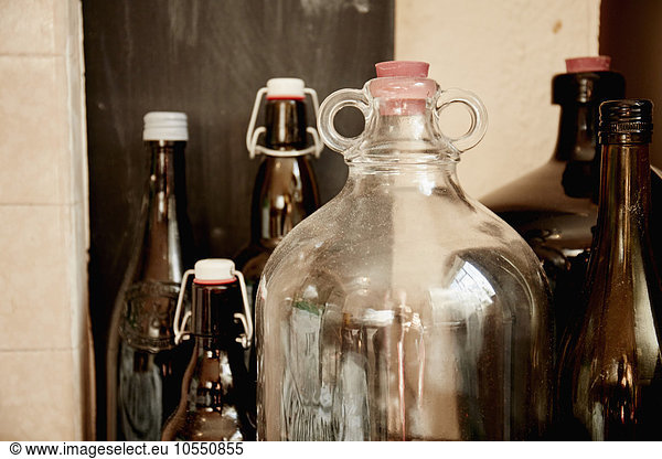 Ein Regal mit Flaschen und Gläsern  ein großes Glas mit doppeltem Henkel und einem Stopfen sowie Flaschen mit Deckel.