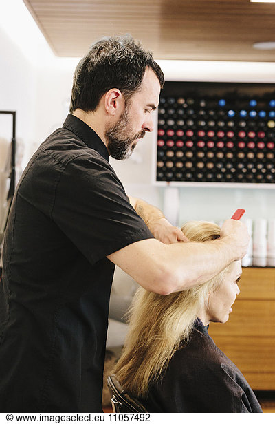 Ein reifer Mann  ein Hairstylist  Colorist  der am Haar einer Frau arbeitet und Haarfarbe auf den Mittelscheitel aufträgt.