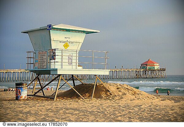 Ein Rettungsschwimmerturm an einem kalifornischen Strand bei Sonnenuntergang. Weit dahinter liegt der Huntington Beach Pier