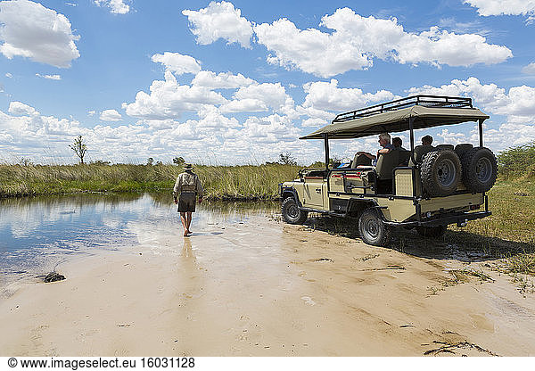 Ein Safari-Fahrzeug mit Passagieren und einem Führer  der über Sand geht