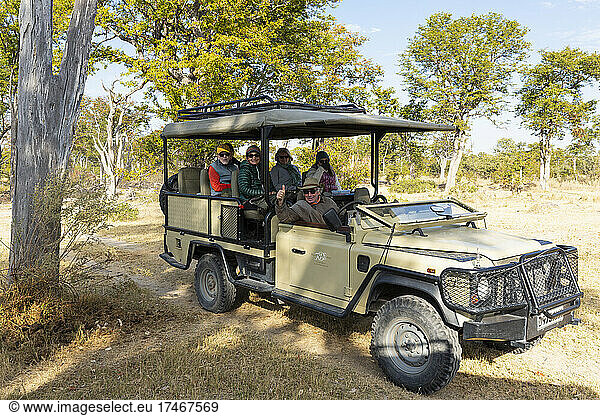 Ein Safari-Jeep, der im Schatten eines Baumes geparkt ist und in dem Menschen sitzen.