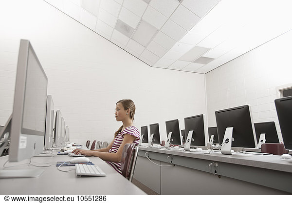 Ein Schulraum  ein Computerraum mit Bildschirmreihen und Sitzgelegenheiten. Eine junge Person  die an einem Terminal sitzt und arbeitet.