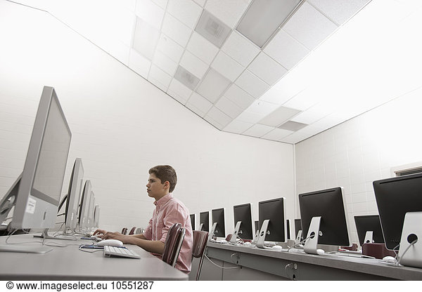 Ein Schulraum  ein Computerraum mit Bildschirmreihen und Sitzgelegenheiten. Eine junge Person  die an einem Terminal sitzt und arbeitet.