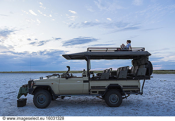 Ein sechsjähriger Junge und seine jugendliche Schwester sitzen in der Abenddämmerung auf einem Safari-Fahrzeug