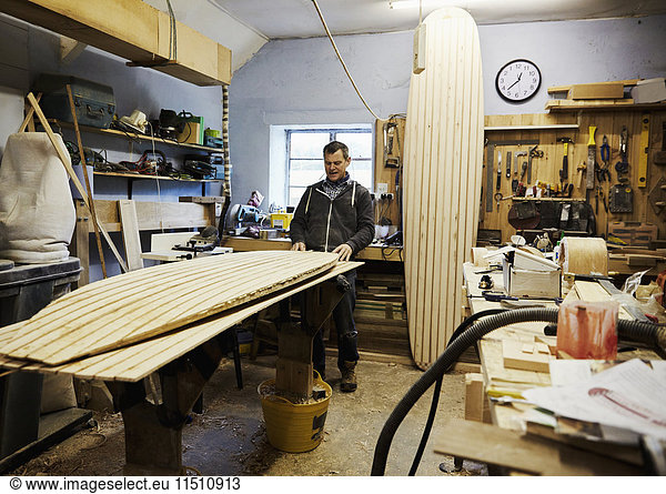 Ein Surfbrett-Workshop  ein langes  aufrecht stehendes Brett und ein Brett in Produktion auf einer Werkbank. Ein Surfbrettmacher bei der Arbeit.