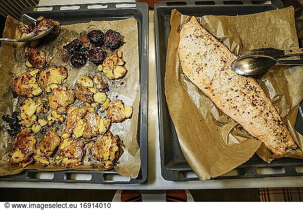 Ein Tablett mit hausgemachtem  gewürztem  im Ofen gebackenem Lachs und zerkleinerten Kartoffeln nebeneinander auf einem Tisch.