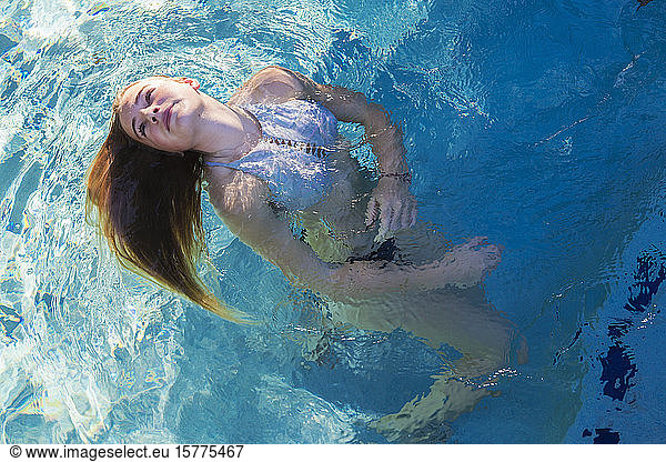 Ein Teenager-Mädchen schwimmt in einem Pool  die Haare mit dem Kopf nach hinten auf dem Wasser ausgebreitet.