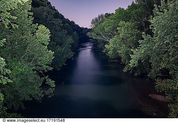 Ein von Bäumen gesäumter Kanal leuchtet blau im sanften Licht der Abenddämmerung