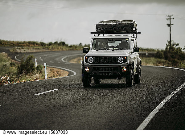 Ein weißer 4x4 mit einem Dachzelt fährt eine Landstraße in Neuseeland