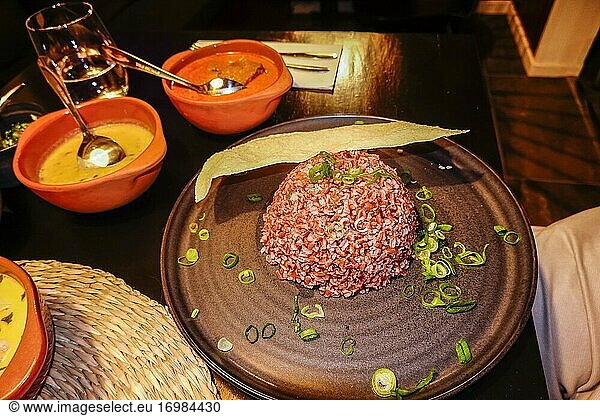Eine Auswahl an sri-lankischen Speisen in einem sri-lankischen Restaurant und ein Haufen roter Reis und Frühlingszwiebeln.