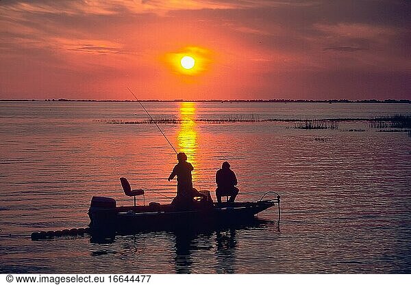 Eine Familie angelt bei Sonnenuntergang auf dem Okeechobe-See in Florida von einem Boot aus nach Barschen.
